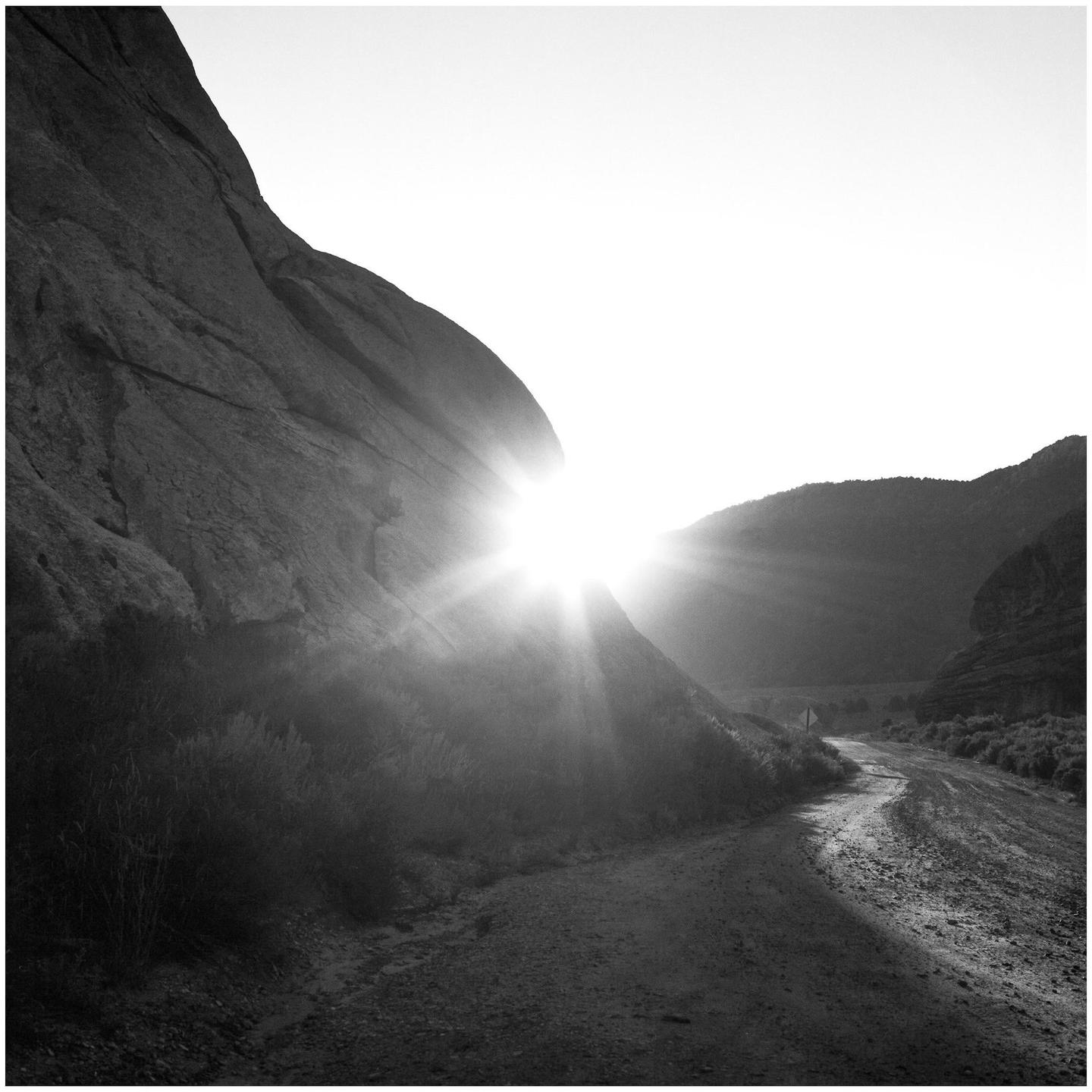 The sun shines brightly over a winding road through a rocky landscape.