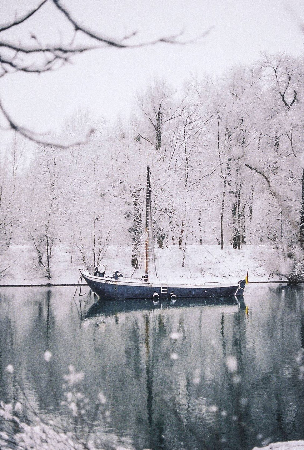 A boat is moored on a body of water surrounded by snow-covered trees.