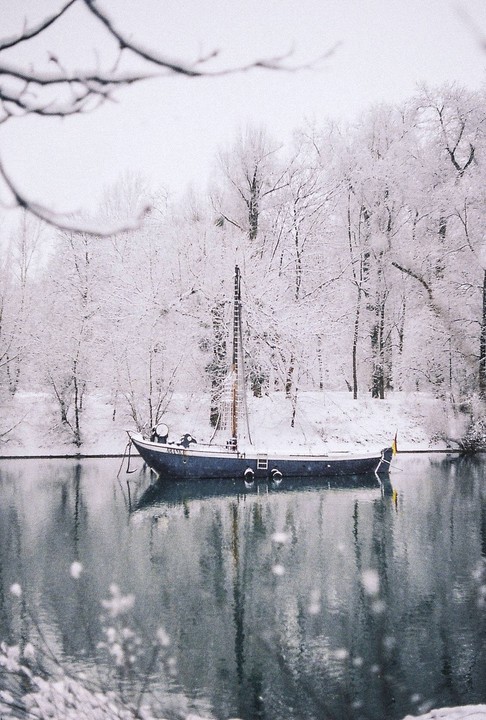 A boat is moored on a body of water surrounded by snow-covered trees.
