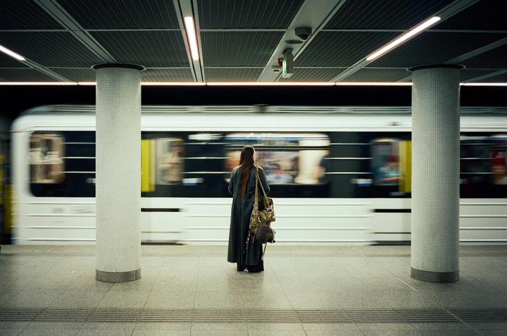 A woman stands on a subway platform as a train passes by.