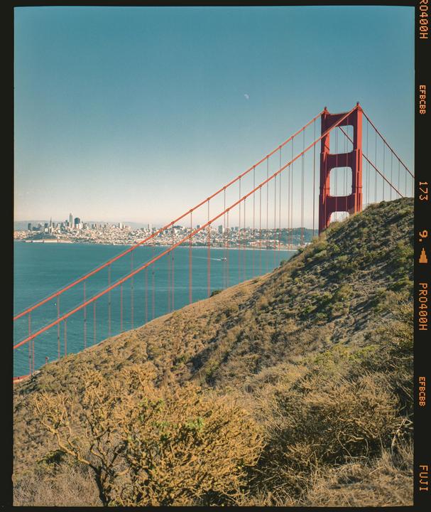 The Golden Gate Bridge is visible from a hill overlooking the water, with a city skyline in the distance.