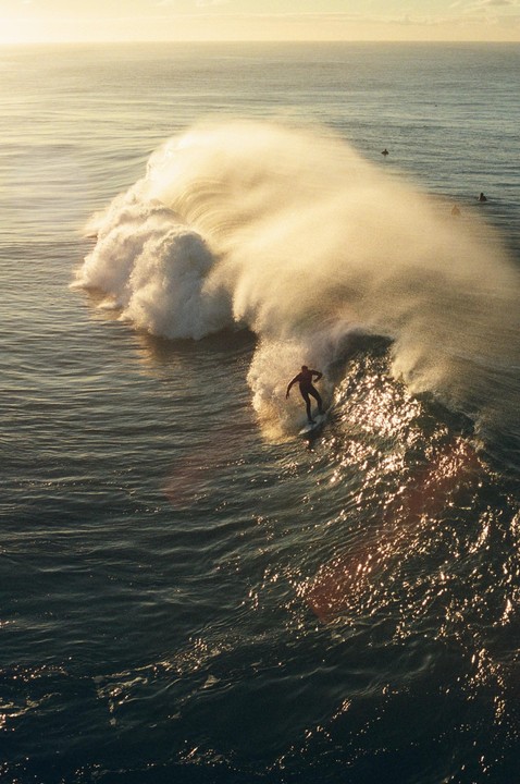 A surfer rides a large wave as the sun reflects on the water.
