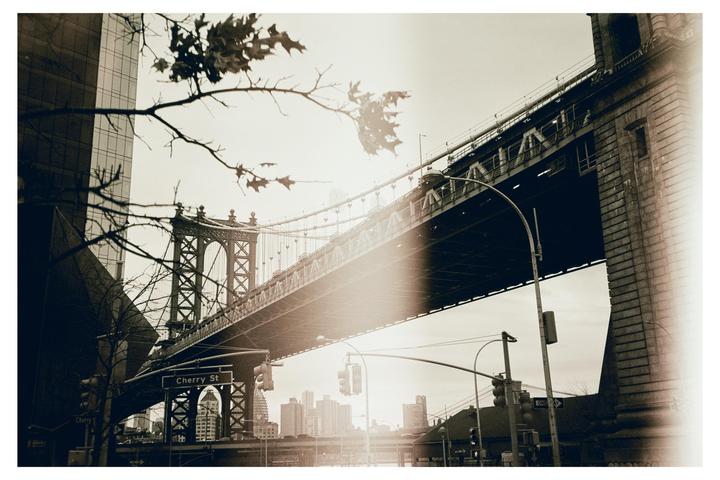 The Manhattan Bridge is seen from below, with a street sign for Cherry Street visible.