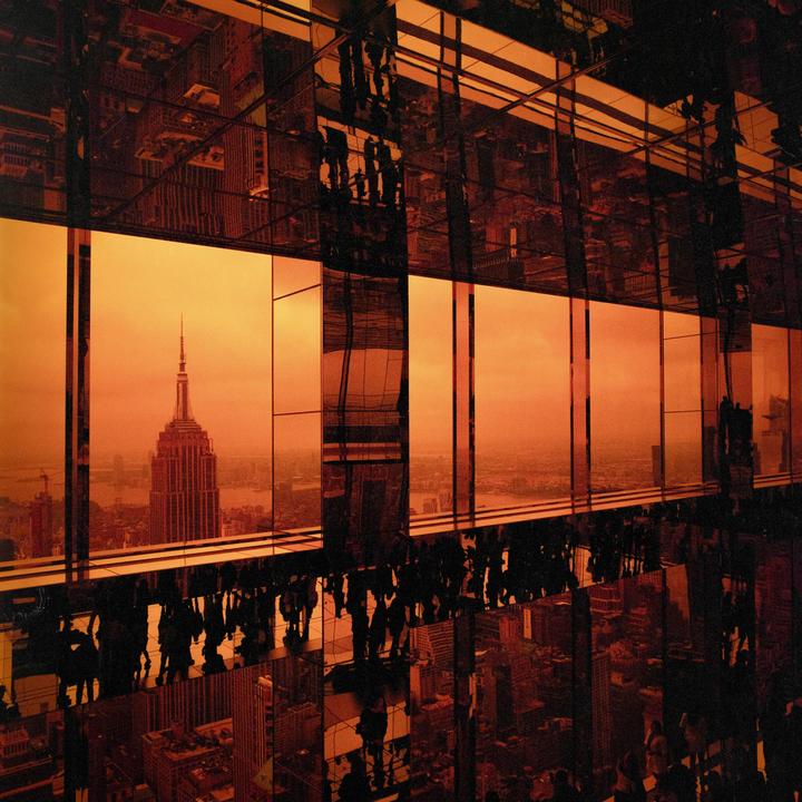 The Empire State Building is visible through a window with reflections of people and city buildings.