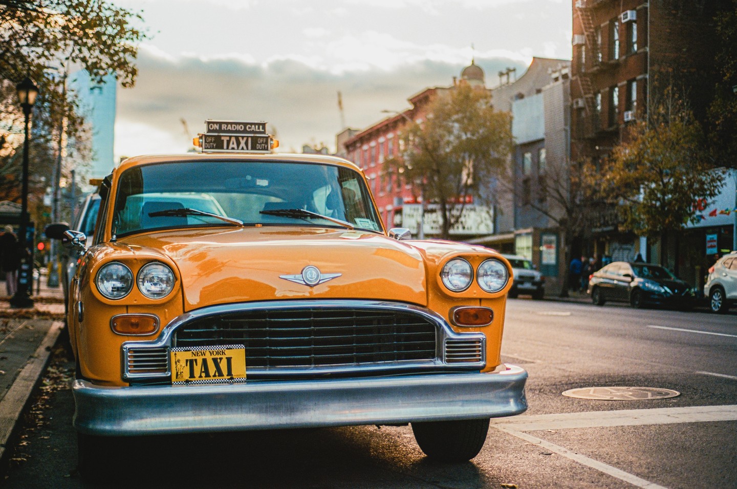 A yellow taxi is parked on a city street with buildings and trees in the background.