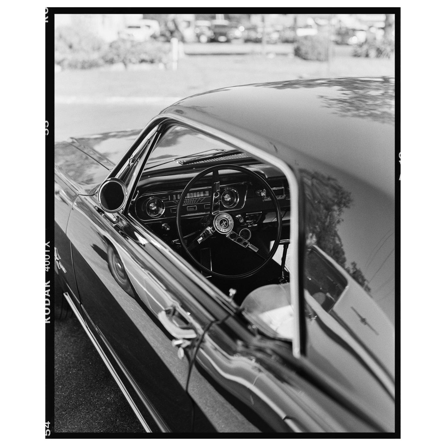 A black and white photograph shows the interior of a vintage car through an open window.