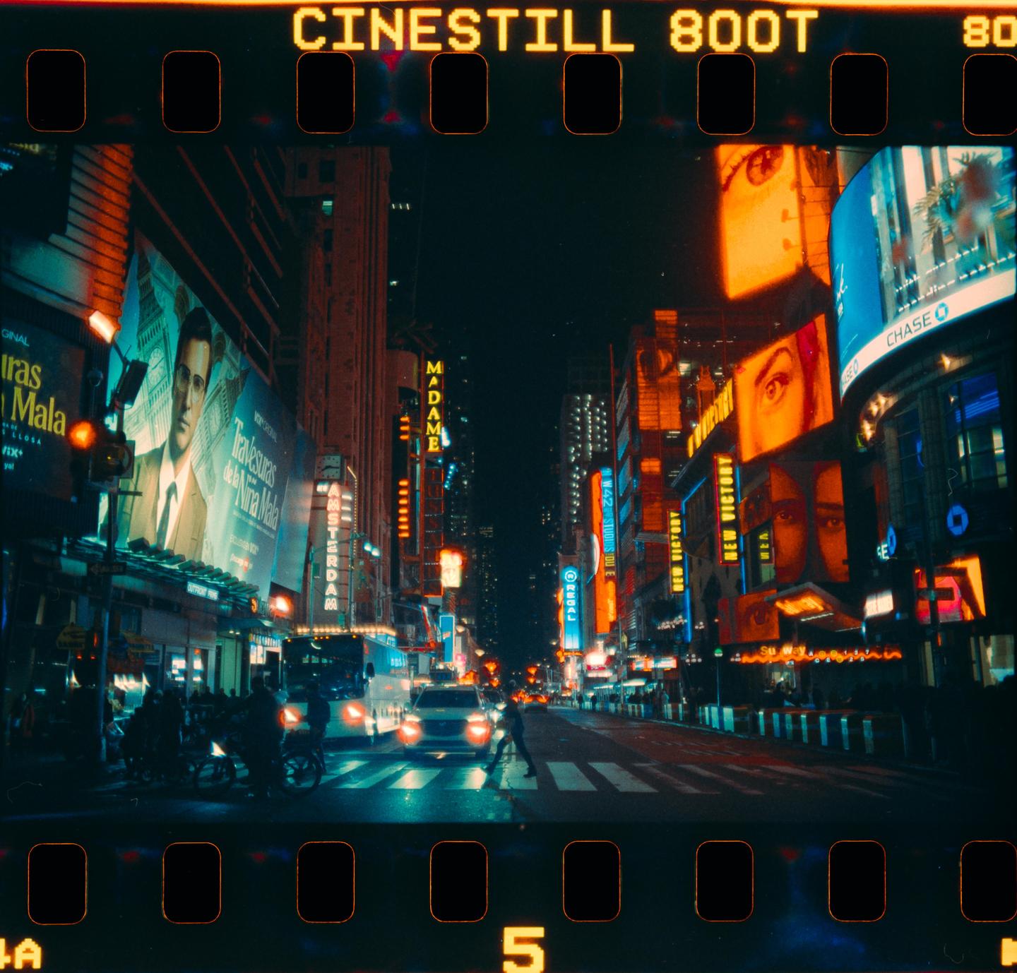 A street at night is illuminated by the neon signs of many buildings and billboards.