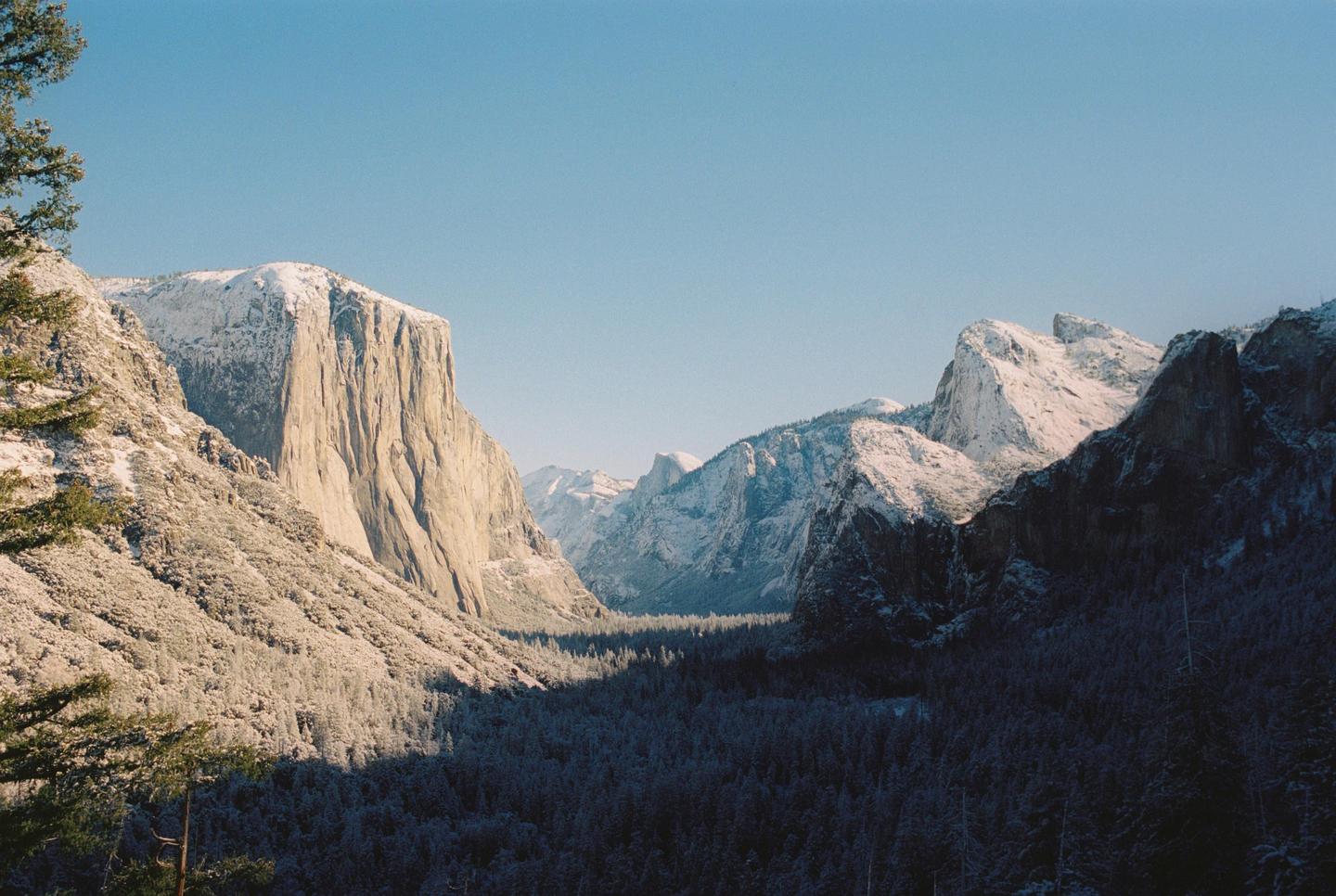 A valley with snow-covered mountains and a forest is visible under a clear sky.