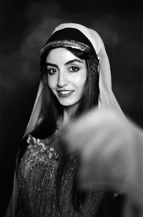 A woman wearing a decorative headpiece and dress smiles at the viewer.