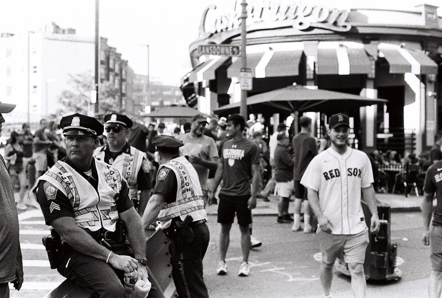 A group of police officers and civilians are gathered on a street in front of a building with an awning.