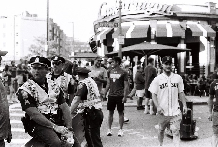 A group of police officers and civilians are gathered on a street in front of a building with an awning.