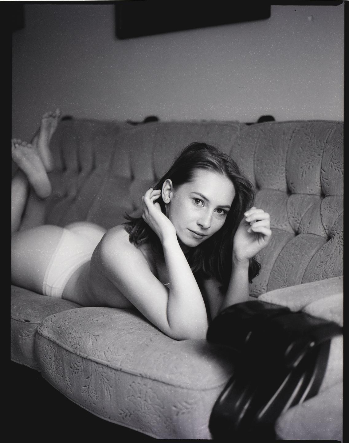 A woman lies on a sofa, looking at the viewer.