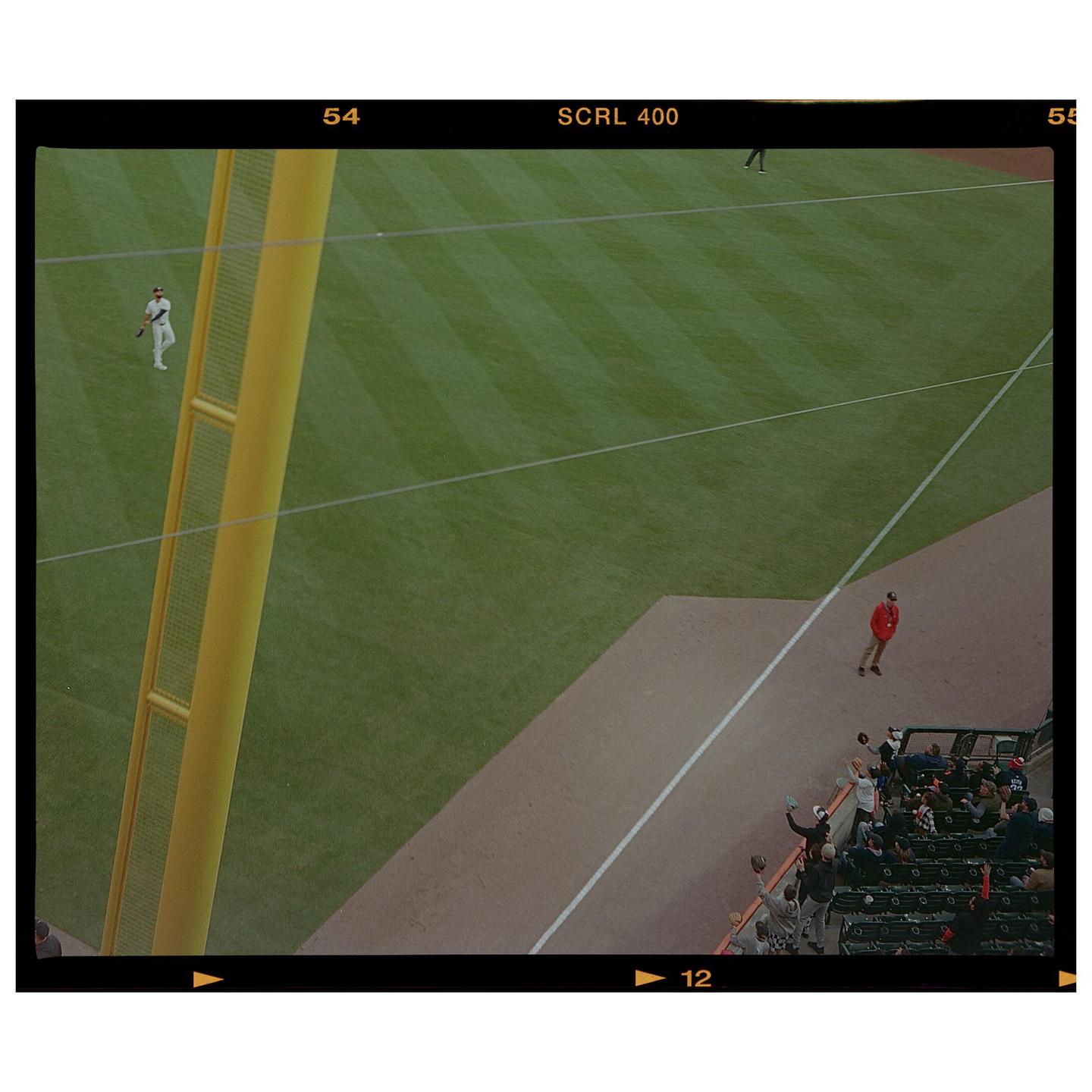 An aerial view shows a baseball field with players and spectators in the stands.