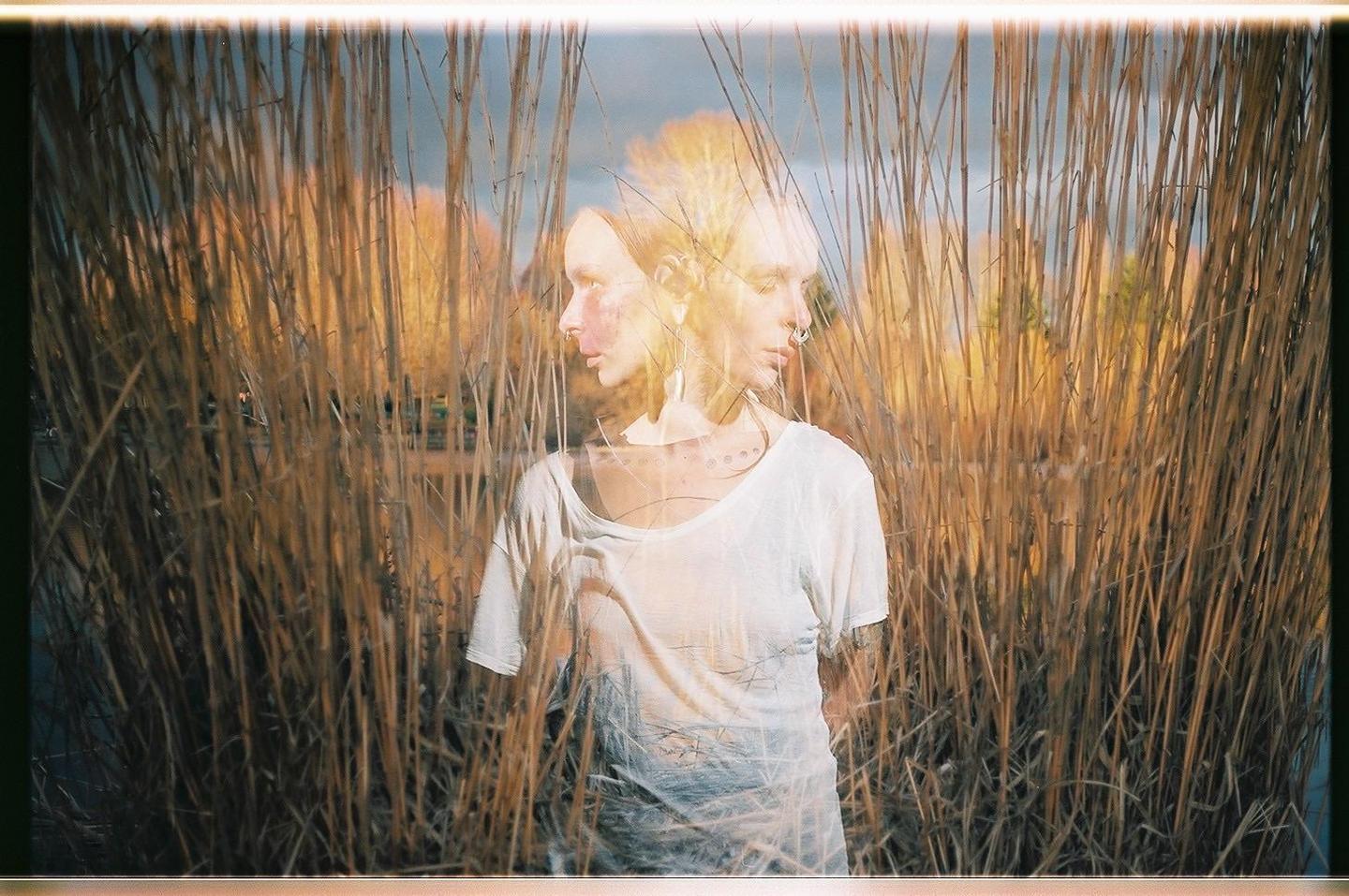 A woman with multiple exposures is visible through tall reeds.
