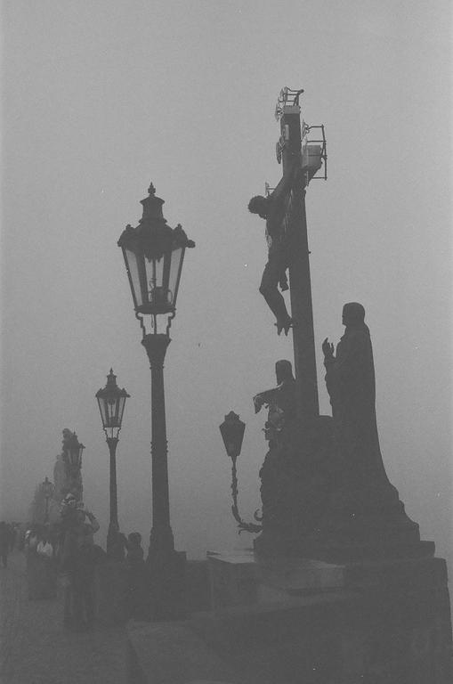 A statue of Jesus on a cross stands next to a street lamp on a hazy day.