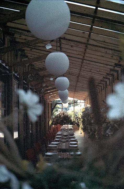 A long table set for a meal is visible in a covered outdoor area with hanging spherical lights.