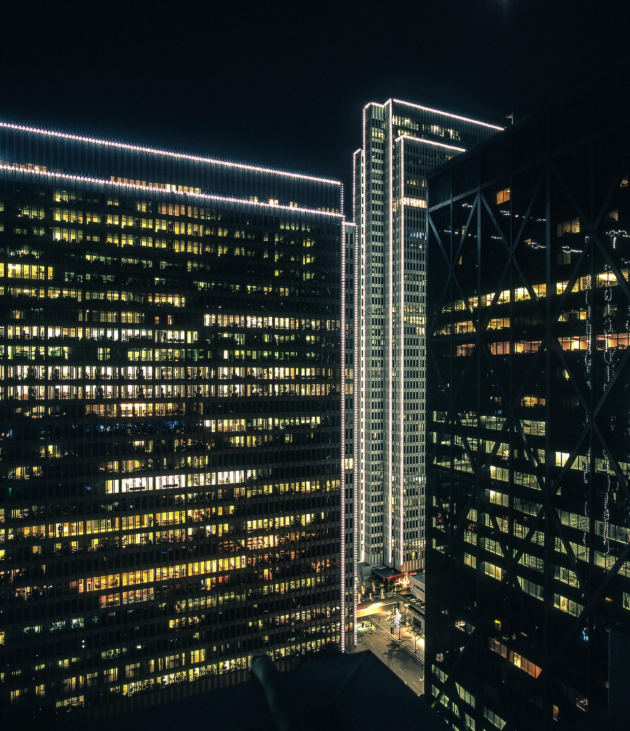 Three tall buildings with many illuminated windows stand against a dark night sky.