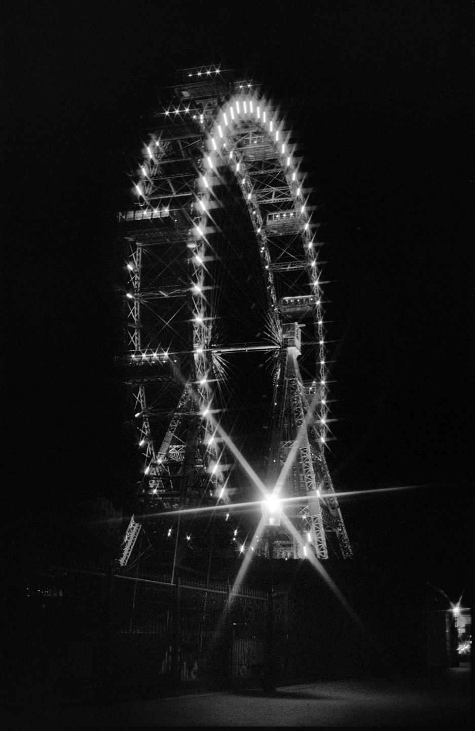 A large ferris wheel illuminated by many lights stands against a dark night sky.