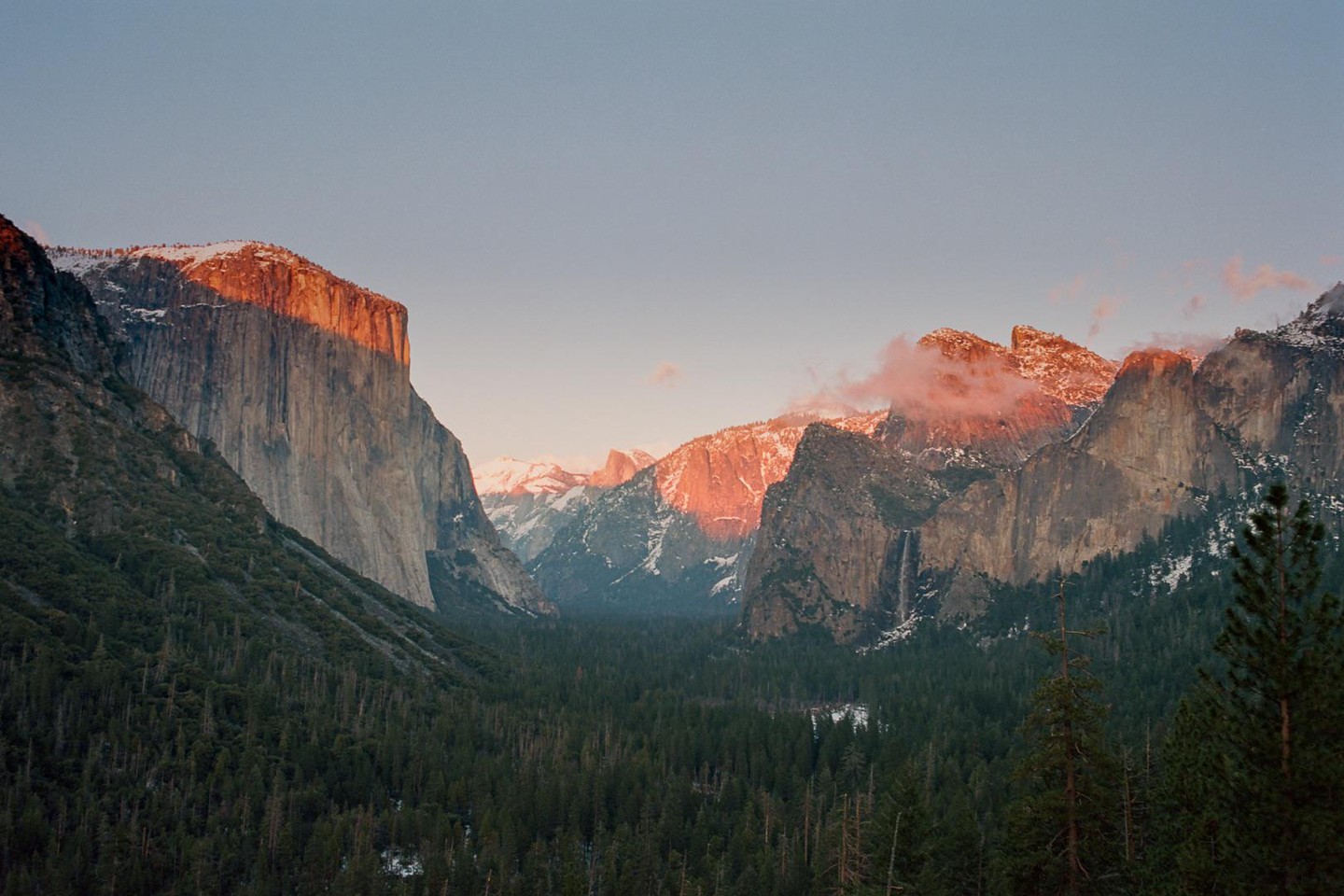A valley with a forest and mountains is illuminated by the setting sun.