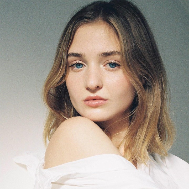 A woman with blue eyes and light brown hair looks directly at the viewer.
