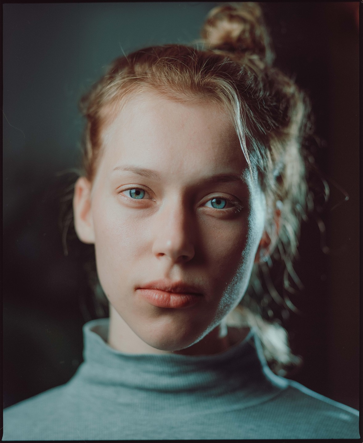 A young woman with blue eyes and a bun looks directly at the viewer.
