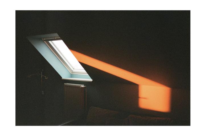 Sunlight streams through an attic window, casting an orange glow on the dark wall.