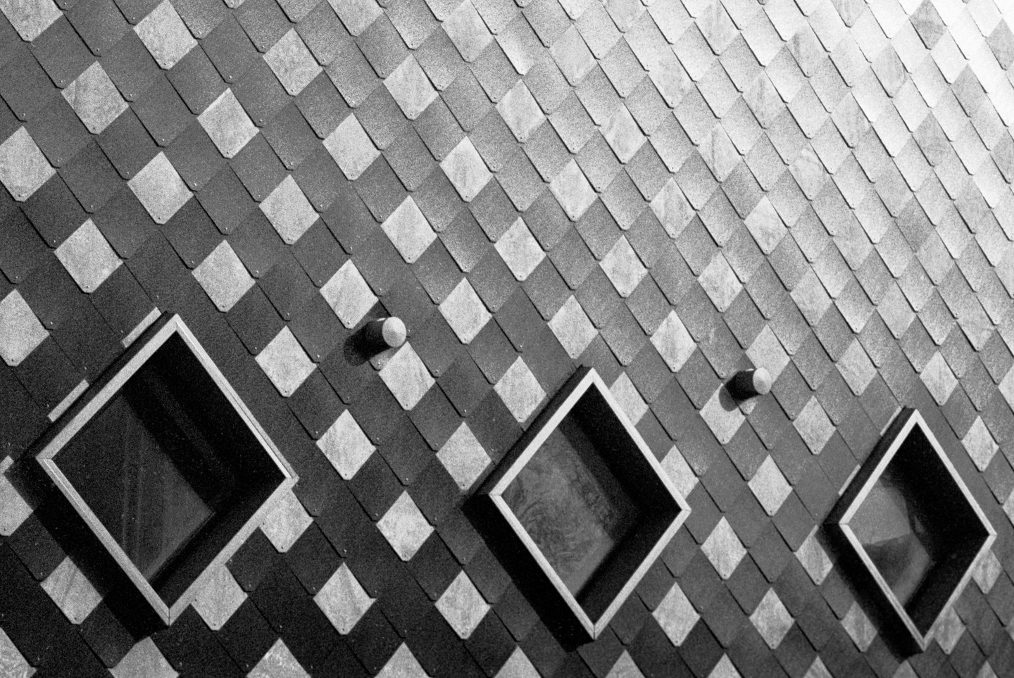 Three square windows are set into a wall covered in diamond-shaped shingles.