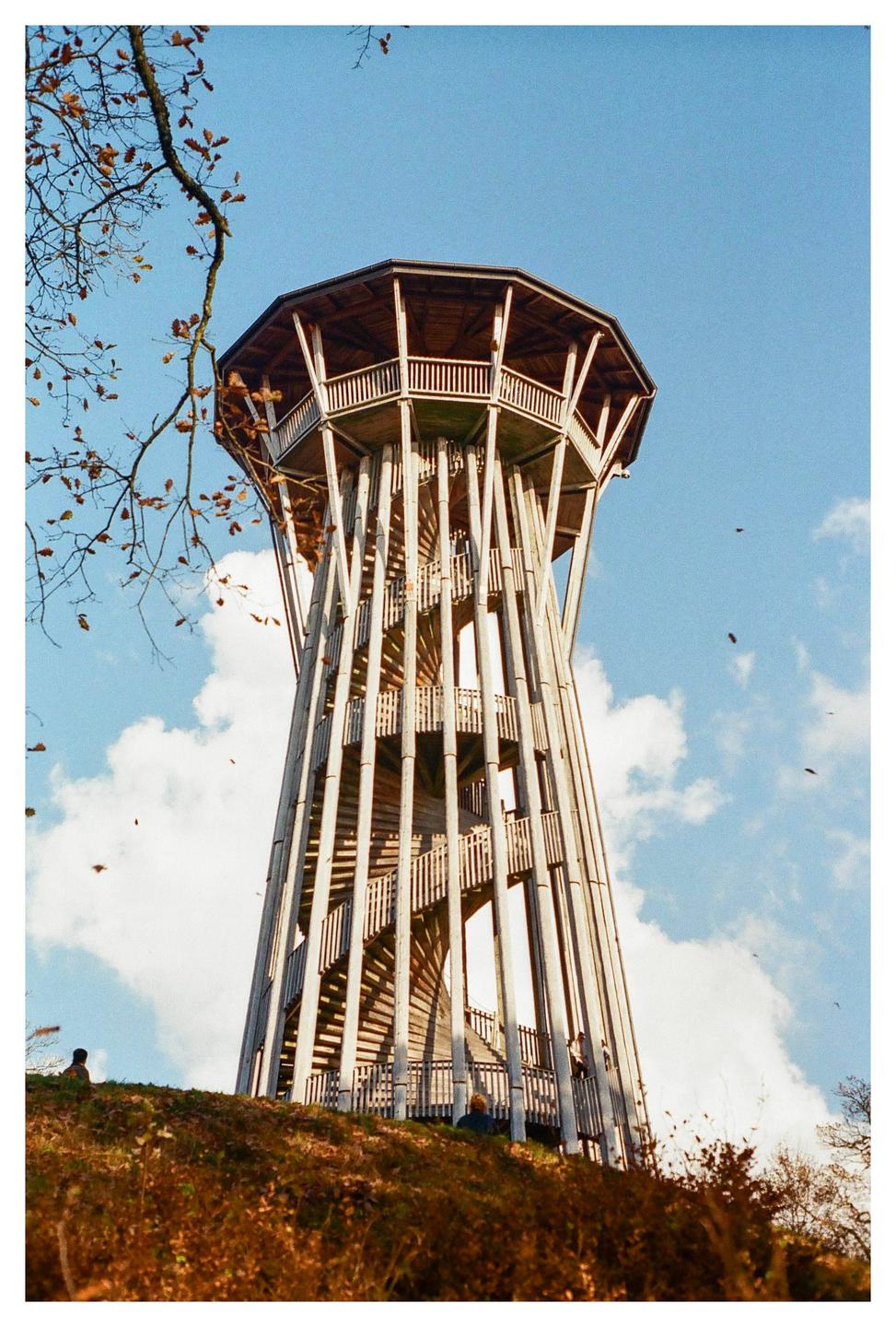 A tall wooden observation tower with a spiral staircase stands against a blue sky with white clouds.