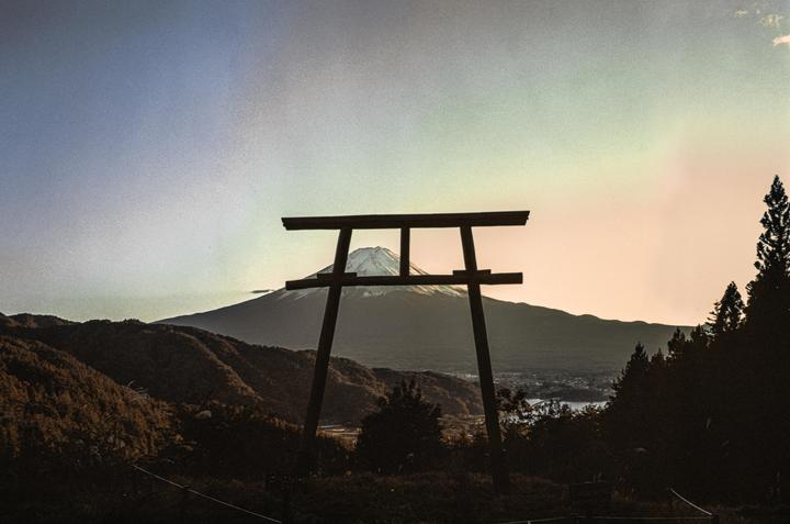 A torii gate stands silhouetted against a mountain with a snow-capped peak and a colorful sky.