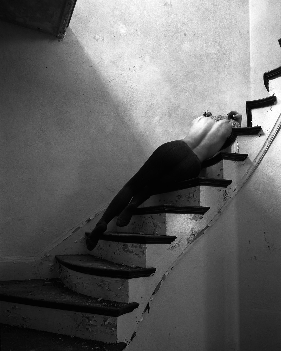 A woman lies on a decaying staircase in an abandoned building.