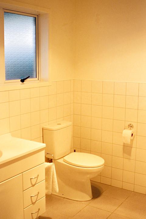 A toilet, sink, and window are visible in a bathroom with tiled walls.