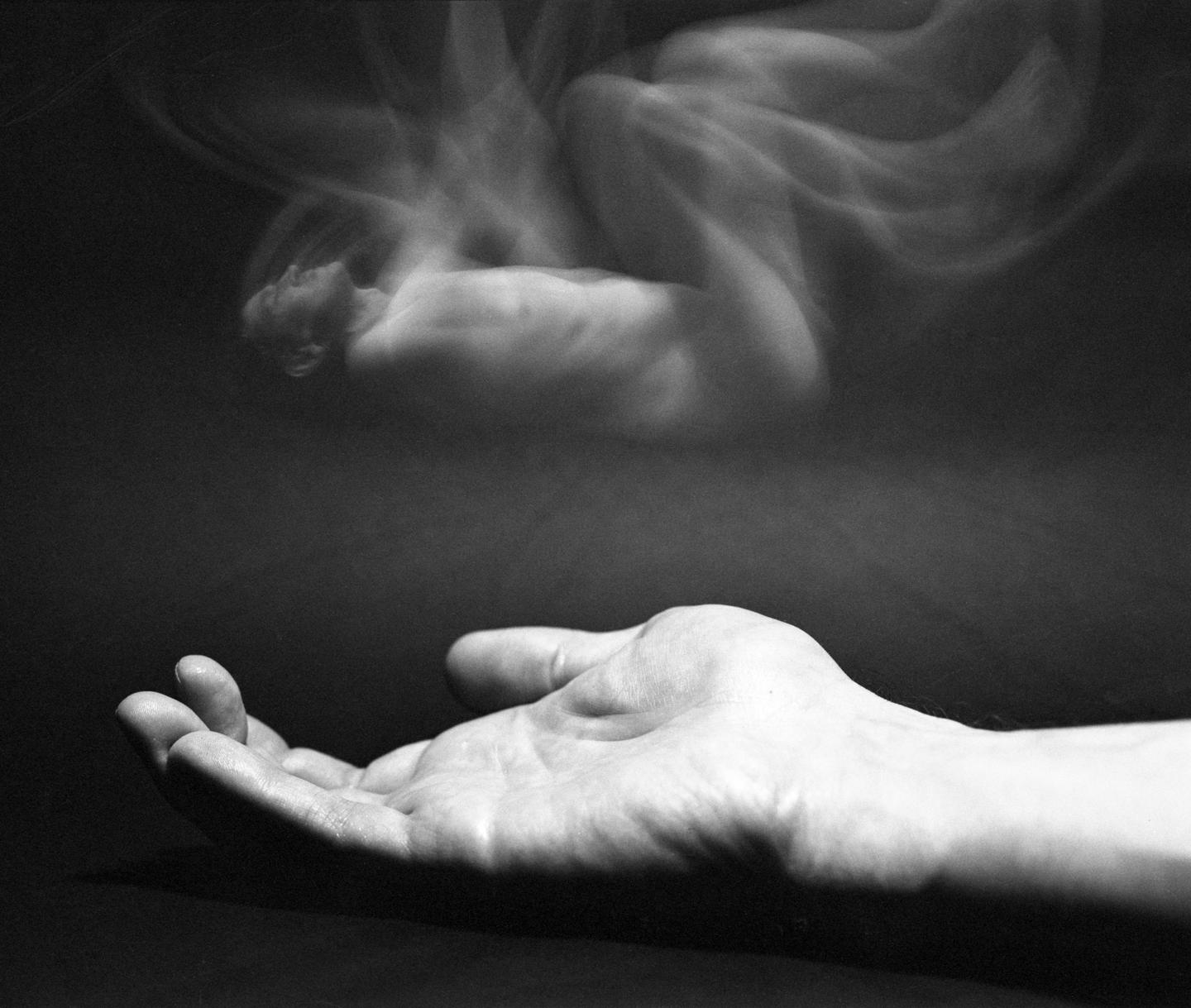 A hand reaches up towards a blurry, ghostly figure of a person floating above it.