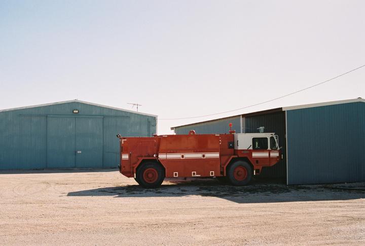 A red and white firetruck is parked in front of a blue building with a large door.