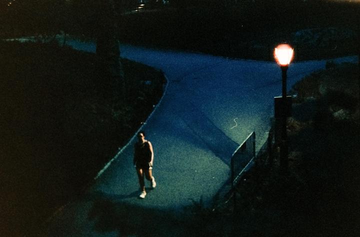A man walks on a winding path at night, illuminated by a street lamp.