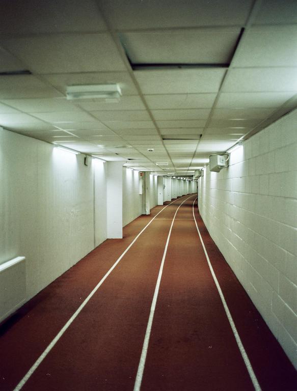 A long, curving indoor running track with white lane lines is illuminated by overhead lights.