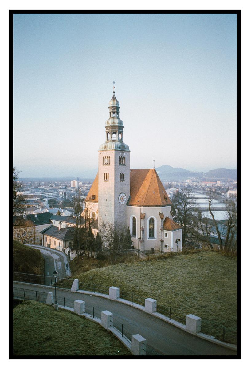 A church with a tall steeple and a red roof stands on a hill overlooking a city.