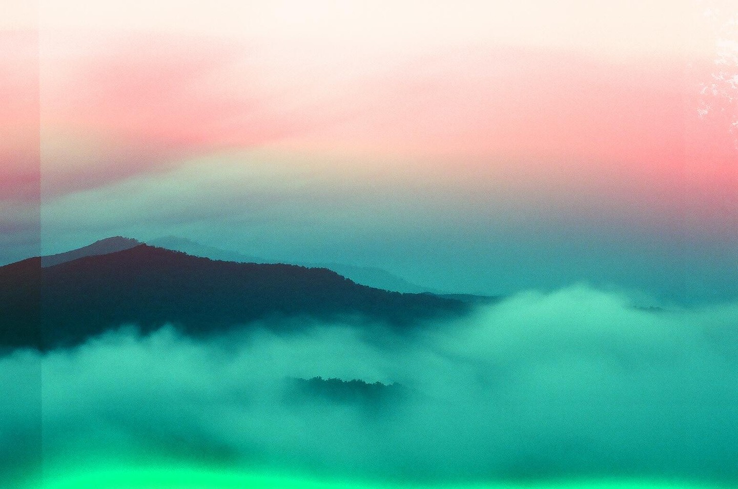 A mountain range is covered in fog under a pink and blue sky.