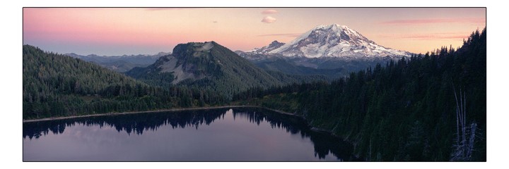 A panoramic landscape shows a lake reflecting a forest and mountains, with a snow-capped peak under a pink sky.