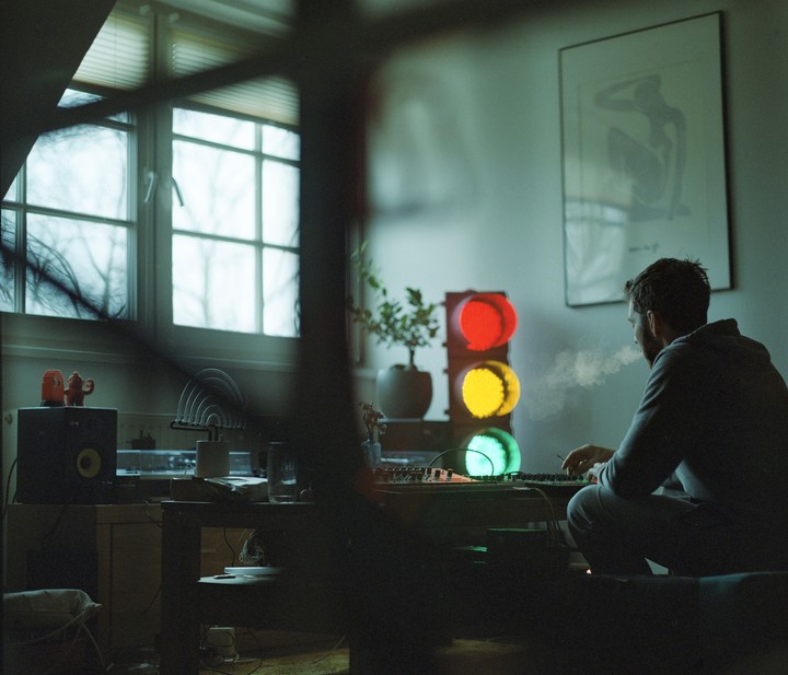 A man sits at a desk with a traffic light next to him, exhaling smoke.
