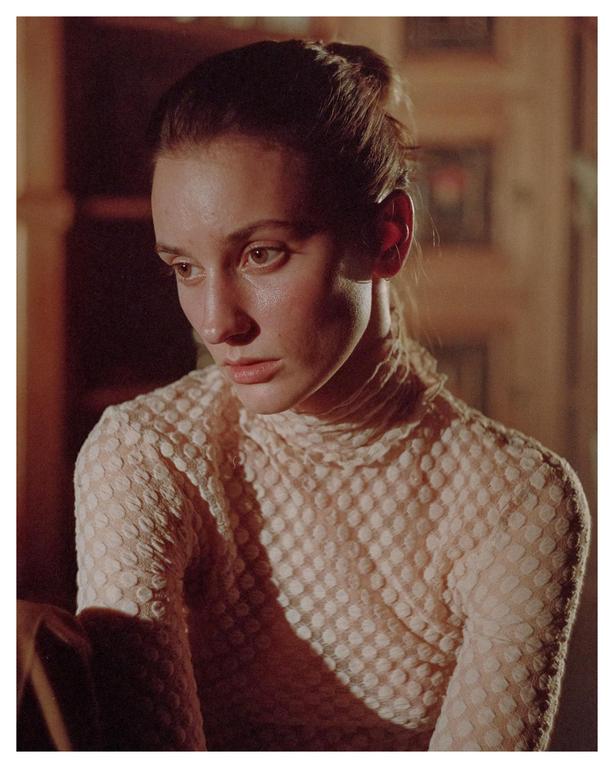 A woman with her hair pulled back looks down and to the side, illuminated by a warm light.