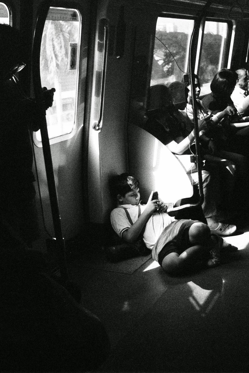 A boy sits on the floor of a train car, looking at his phone.