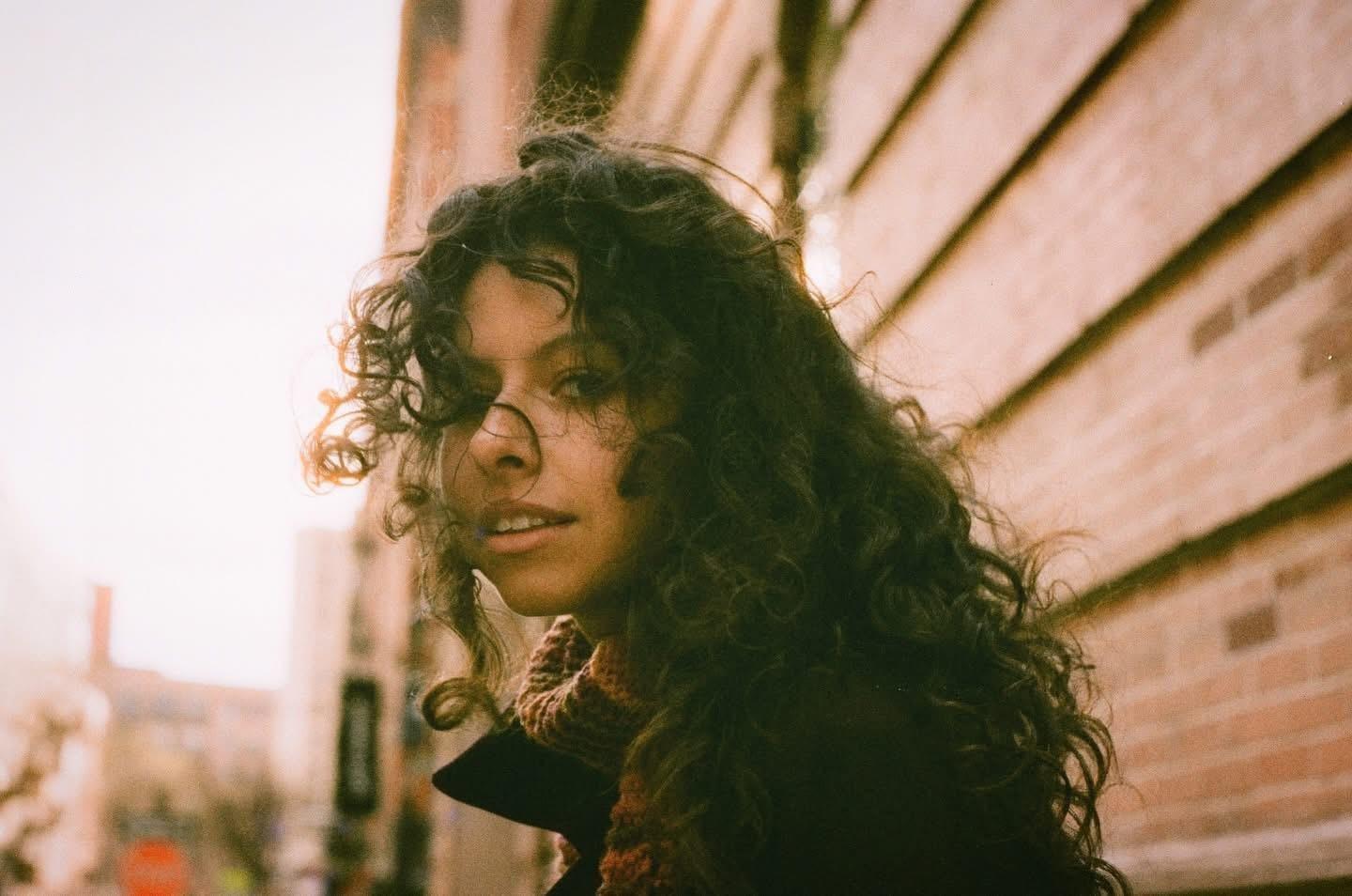 A woman with long curly hair looks over her shoulder at the viewer.