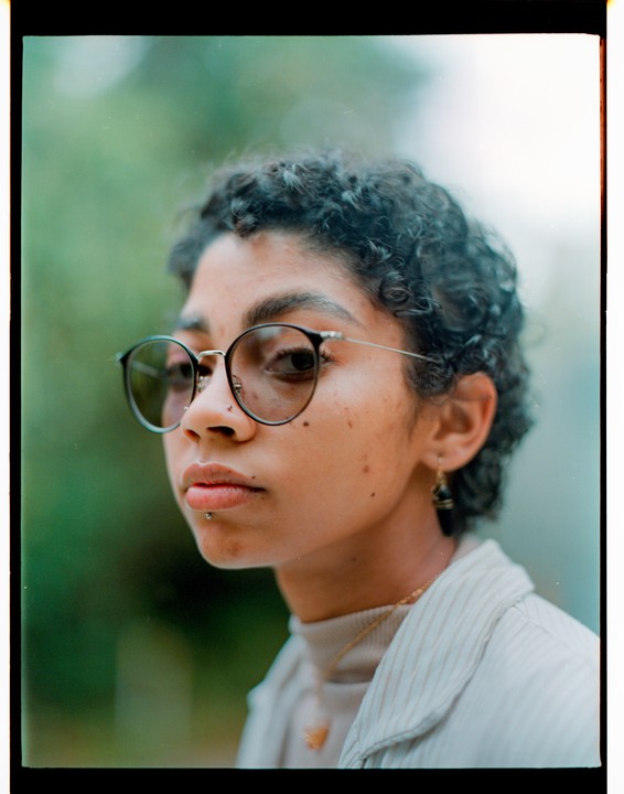 A woman with curly hair and glasses looks to the side in a close-up portrait.