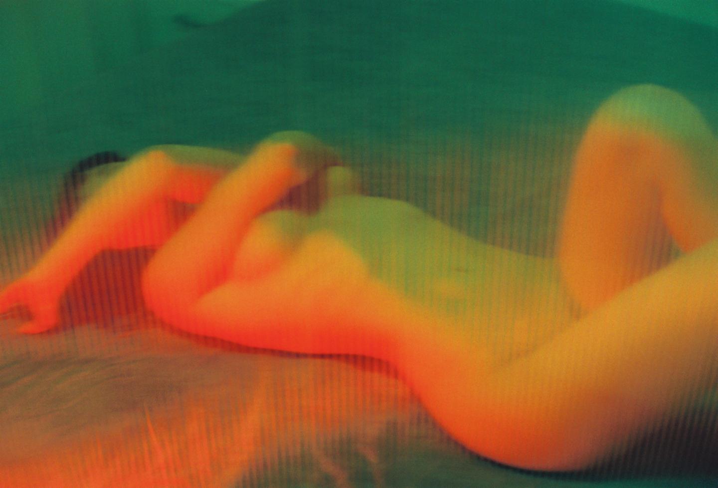 A woman is lying on a bed with her arms above her head, illuminated by red and green light.