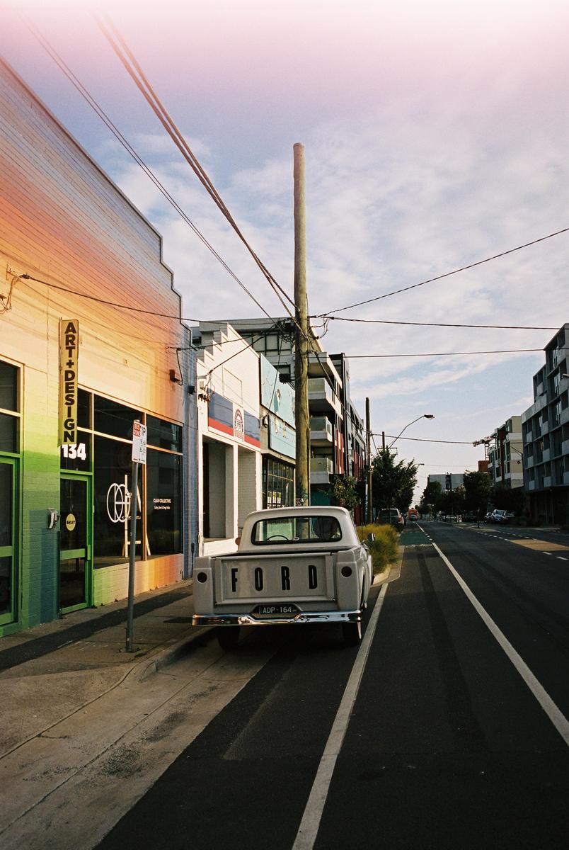 A white Ford pickup truck is parked on the side of a street next to a building with "ART+DESIGN" written on it.