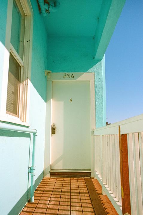 A white door with the number 4 is visible on a building with turquoise walls and a wooden slatted floor.