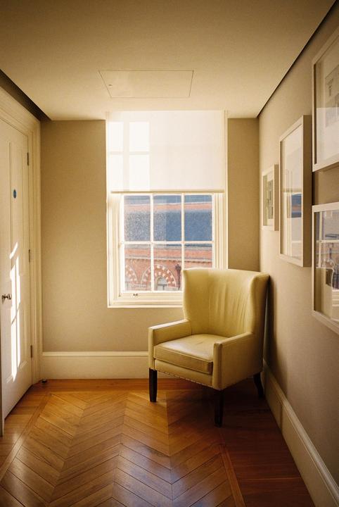 Sunlight streams through a window onto a yellow armchair and a wooden floor with a herringbone pattern.
