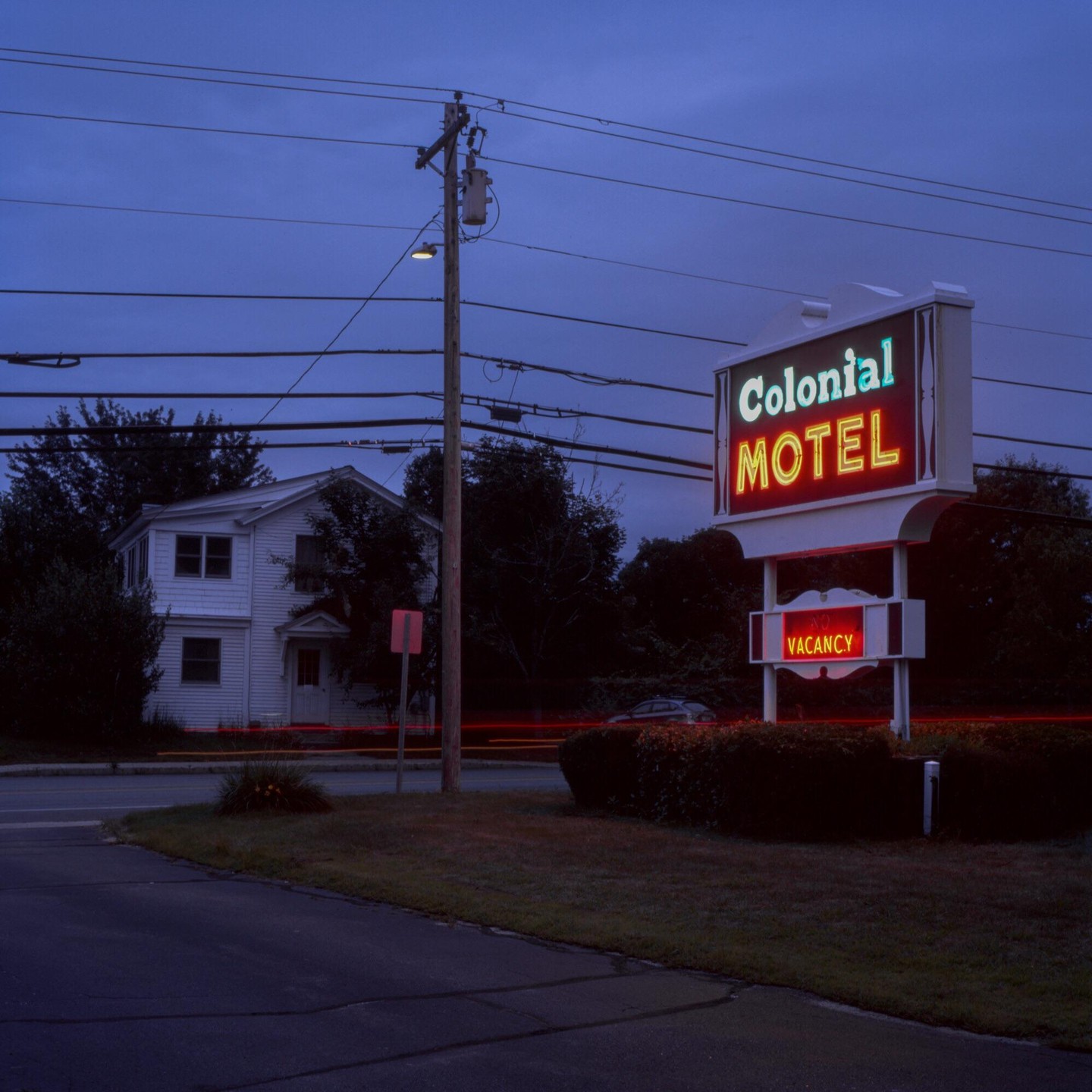 A neon sign for the Colonial Motel with a "Vacancy" sign is visible at night next to a road and a white house.