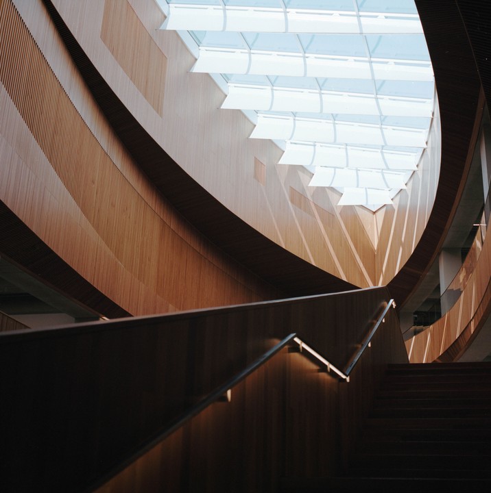 A wooden staircase with a metal handrail curves upwards towards a skylight.