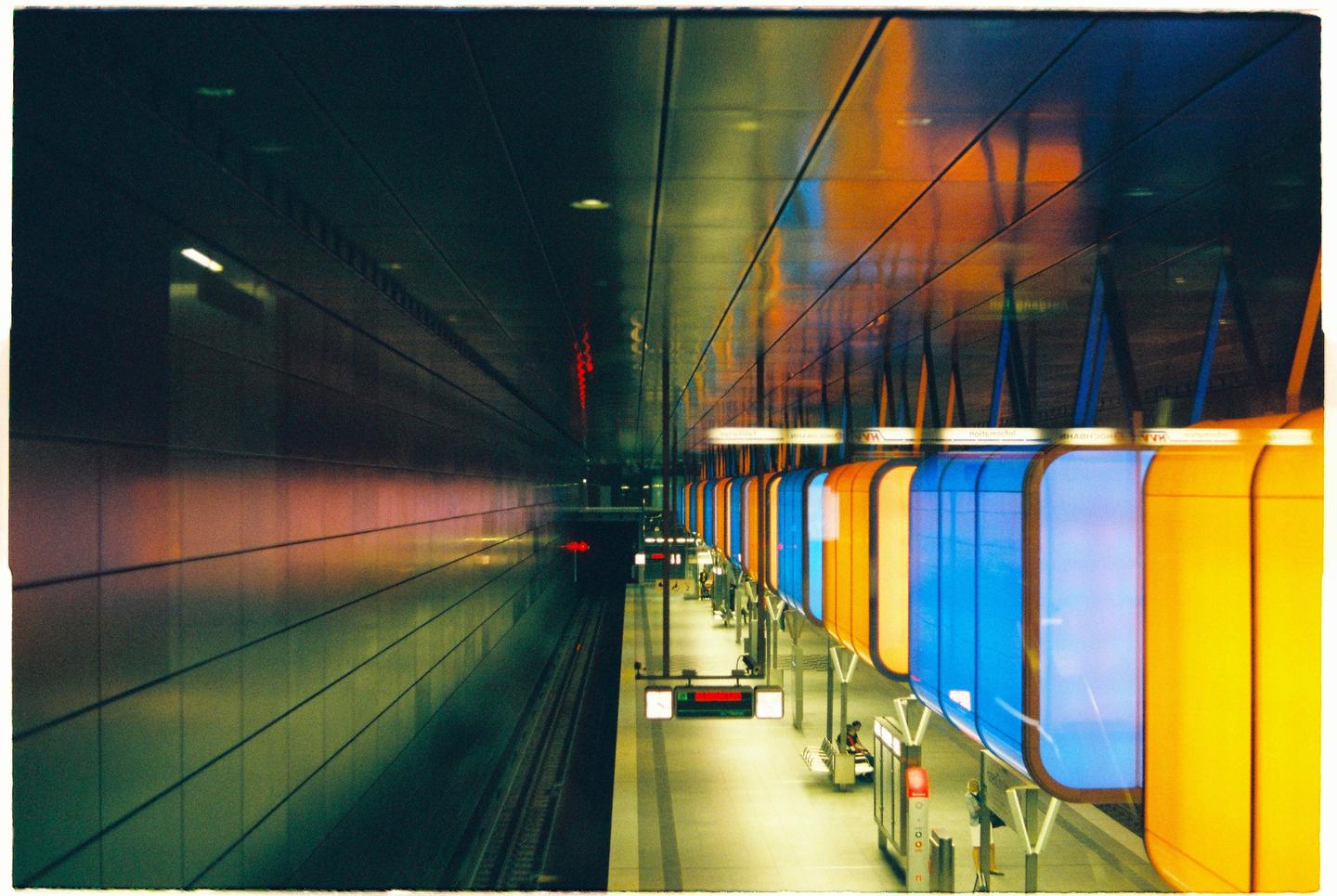 A long exposure shows a subway platform with colorful blue and orange panels and a train track.